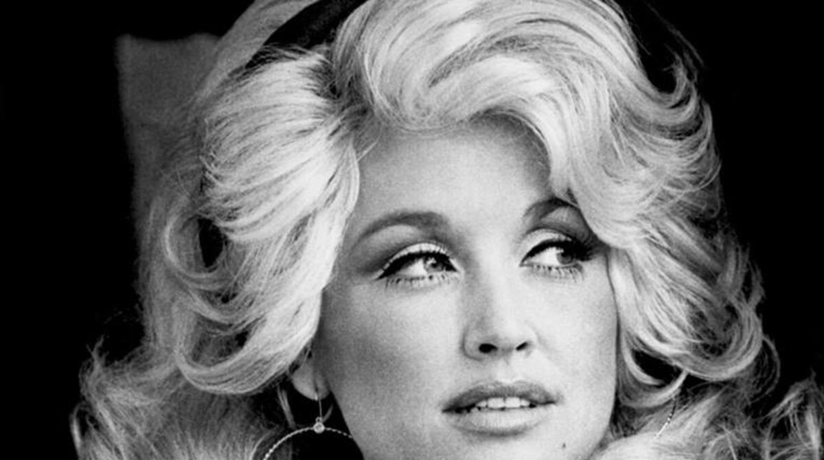 Dolly Parton in a publicity photo from 1977, wearing a denim shirt with her hair styled in her signature big blonde curls