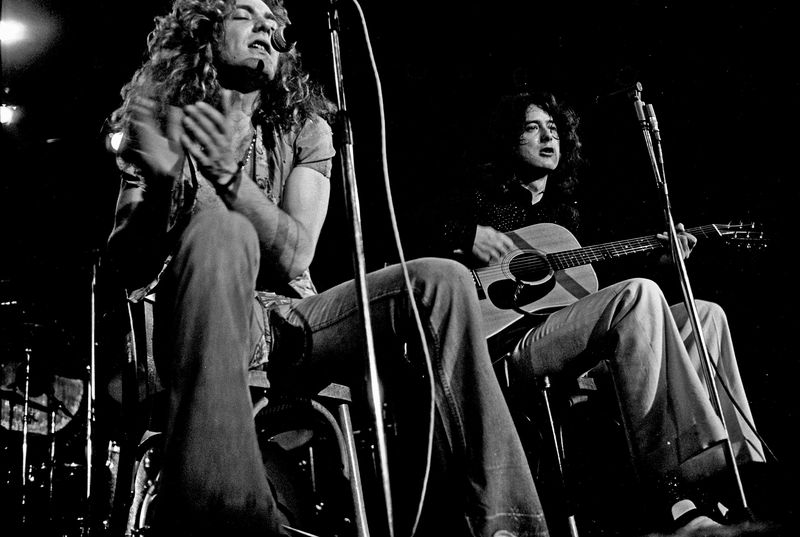 Robert Plant seated and clapping beside Jimmy Page with an acoustic guitar during an acoustic set in Hamburg, Germany, in 1973