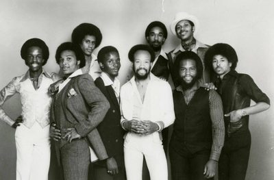 Earth, Wind and Fire in a black and white 1977 Columbia Records press photo, nine members standing close together, the Earth Wind and Fire songs lineup
