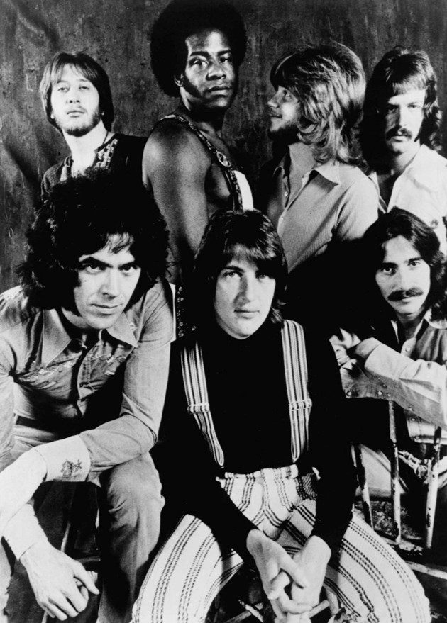 Black and white 1972 portrait of the seven members of Three Dog Night posed together against a dark backdrop, the group behind Black and White and Joy to the World